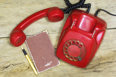 Old Red phone, Paper Notebook and Pen on a Wooden Table. Image is Retro Filtered.の写真素材
