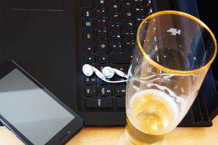 Glass of beer, laptop computer and smartphone on table.の写真素材