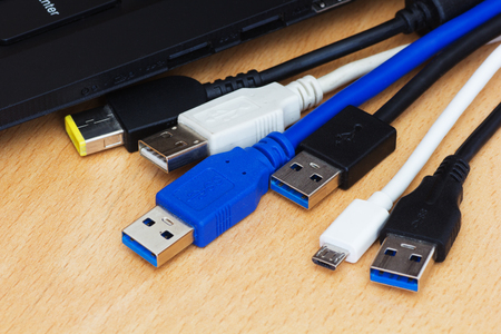 Many diferent usb cables and laptop on wooden background.
