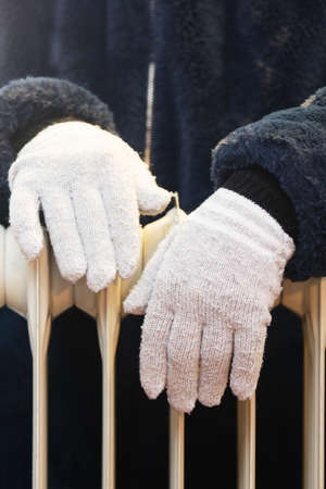 Women's hands in wool gloves over a heating radiator. Focus on hands. Concept of heating season.の写真素材