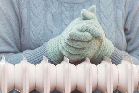 Women's hands in wool gloves over a heating radiator. Focus on hands. Concept of heating season.の写真素材