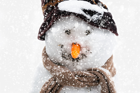 Smiling snowman with carrot nose, hat and scarf. It is snowing around him.の写真素材