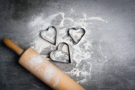Flour, cookie cutters shaped as heart and wooden rolling pin on a gray concrete stone table