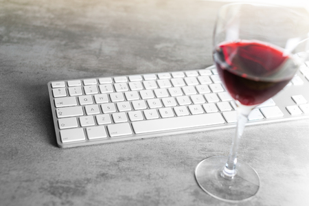 Red wine and computer keyboard on a gray concrete table with focus on the keyboard