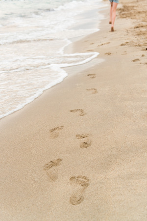 Young girl running on the beach leaving footprints in the sandの写真素材