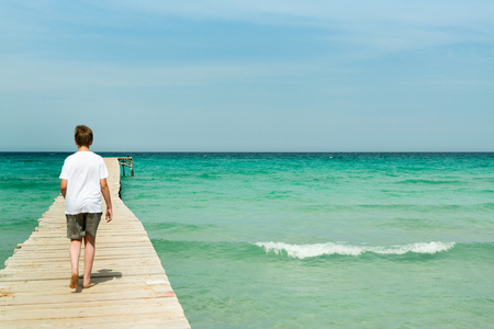 Young man walking on a long wood pier and look over the oceanの写真素材