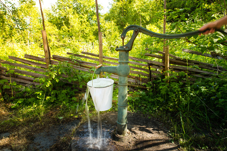 Old retro hand water pump outside in the garden. A hand is pumping and you can see the motion.の写真素材