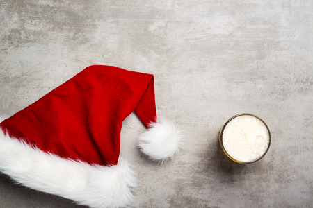 Red santa hat and a glass of beer on a concrete tableの写真素材