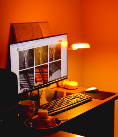 Comfortable workplace with computer, coffee cup and books on orange background