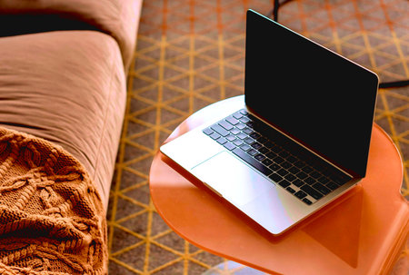 Laptop with blank screen on orange sofa in the living room.