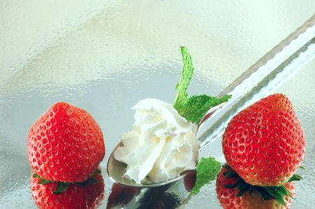Fresh chilled strawberries with whipped cream and mint on a reflective background with a shallow depth of fieldの写真素材