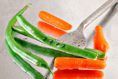 Fresh green beans and  carrots pierced with a fork on a reflective watery mirrored background の写真素材