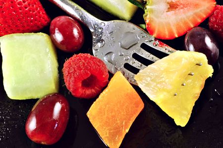 Variety of fresh fruit for a salad on a watery black plateの写真素材