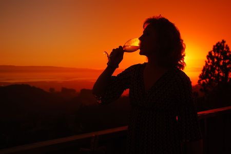 Beautiful middle aged woman drinking a glass of white wine on her deck at sunset