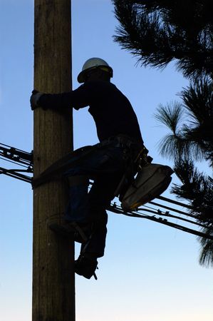 Silhouette of an electrician climbing a newly installed utility poleの写真素材