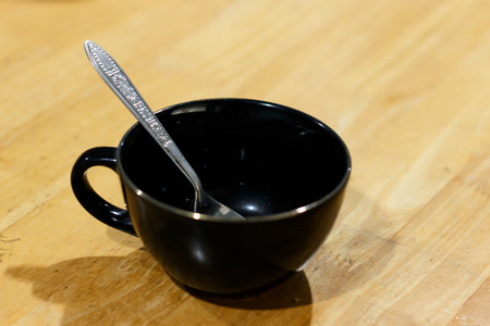 black cup and silver spoon on wood table photo soft focusの写真素材