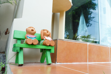 mini doll boy and girl sit at green chair in front of houseの写真素材