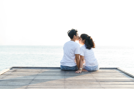 Young man kissing woman on the forehead and sitting at wooden bridgeの写真素材
