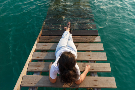 Woman lie at wooden stair into the sea and looking forward.