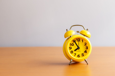 yellow alarm clock on wood table and clear background