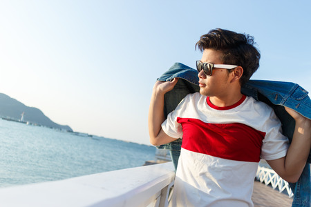 young asian handsome man standing and smile with jean jacket at Asdang bridge on sea background Thailandの写真素材