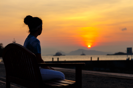 silhouette young woman sitting wood chair waiting for somthing at beautiful sunset backgroundの写真素材