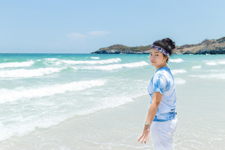 Young asian woman blue and white shirt stand at beach and turn backの写真素材