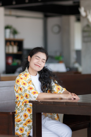 asian woman wear white t-shirt and yellow shirt sitting at wooden chairの写真素材