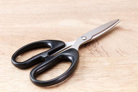 silver scissors and handle is black on wooden floor
