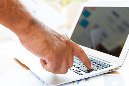 close up business man push enter button of black keyboard laptop and paper on wooden tableの写真素材