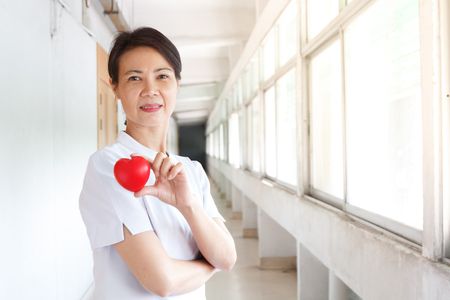 asian nurse in white uniform holding red heart beat with her handsの写真素材