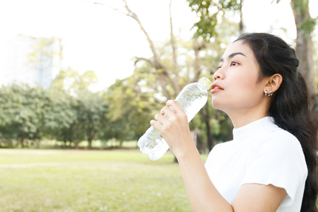 close up beauty asian woman drinking water from bottle on park blur backgroudの写真素材