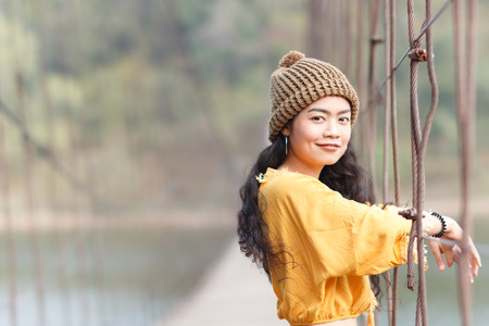 Beauty asian woman in yellow wear and black jeans and wool hat on the wooden bridge