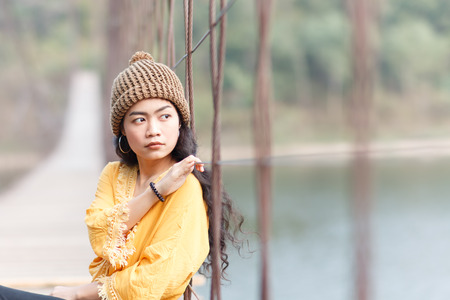 beauty asian woman in yellow wear and black jeans and wool hat on the wooden bridge