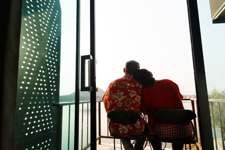 asian elderly couple travel smilling, wear glasses and red shirt  together at terrace and sunlightの写真素材