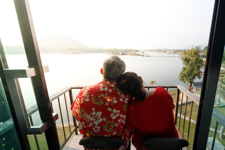 asian elderly couple travel smilling, wear glasses and red shirt  together at terrace and sunlightの写真素材