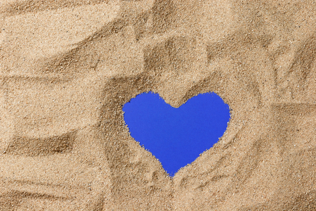 close up sand of beach and have shape of heart on blue paper background from top viewの写真素材