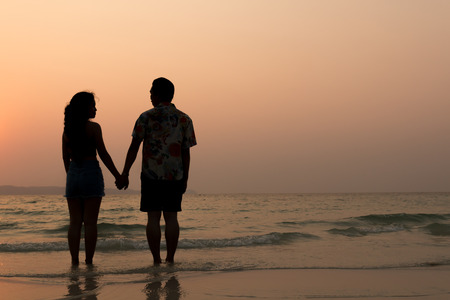 couple asian man and woman holding hand on the beach silhouette at sunsetの写真素材