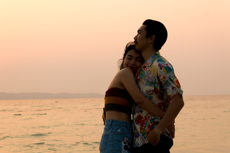 couple asian man and woman hugging on the beach silhouette at sunsetの写真素材