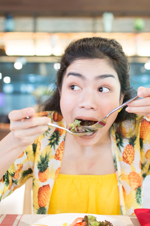 beauty asian woman with yellow wear eating salad with funny moment in restaurantの写真素材