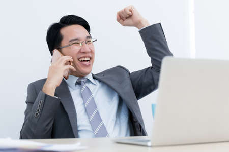 asian business man sitting celebration in office and use smartphone, success conceptの写真素材