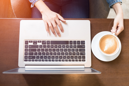 close up hand of business asian woman typing at laptop keyboard in coffee shop from top view with light effect and vintage toneの写真素材