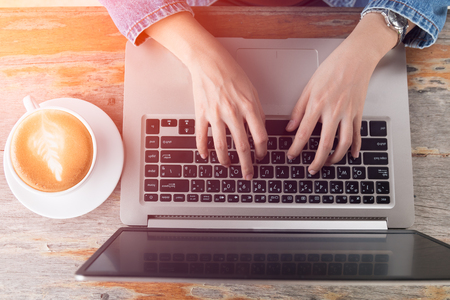 business asian woman typing at laptop keyboard on wooden table and white cup of latte art with light effect and vintage toneの写真素材