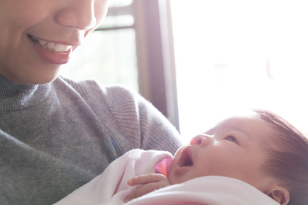 asian mother holding newborn daugther and smiling with her