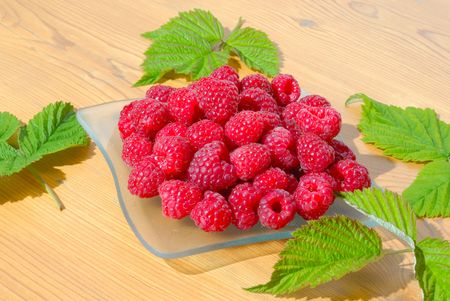 Raspberries with leaves on a wooden table.