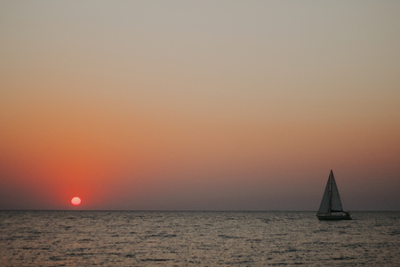 Minimal sun in the setting sun on the sea with a sailboatの写真素材