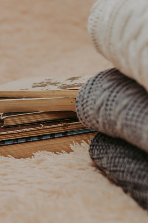 Folded knitted woolen sweaters, stack of old books on a cozy fluffy beige blanket - Imageの写真素材