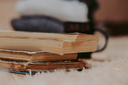 Folded knitted woolen sweaters, stack of old books on a cozy fluffy beige blanket - Imageの写真素材