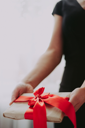 The girl is holding a gift with a red ribbon. A woman in a black dress on a white background is holding a box with red cans.の写真素材
