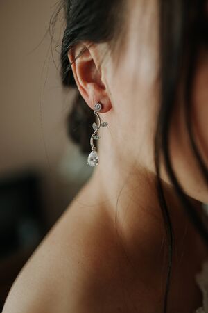 Wedding day. Wedding earrings on a female hand, she takes the earrings, the bride fees, morning bride, white dress, wear earrings. Earrings close-up in the hands of the bride. jewelry accessoriesの写真素材